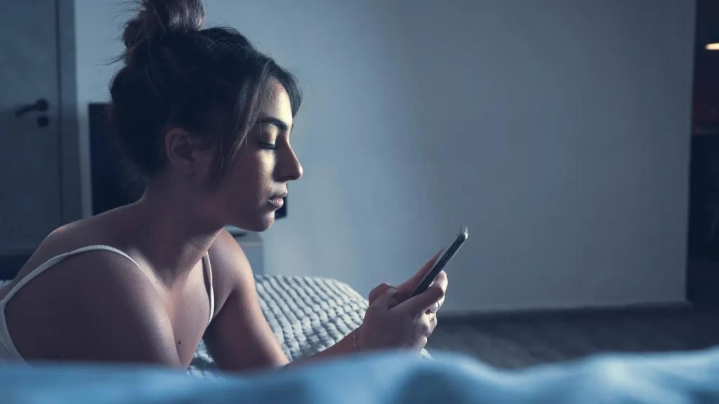 Person lying in bed, looking at their phone in a dimly lit room