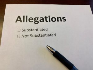 Paper with the world allegations listed at the top and pen resting on it.