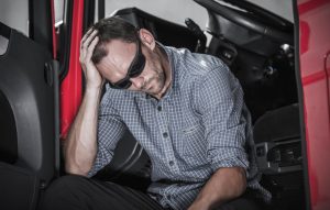 Man sitting in a vehicle looking distressed with his hand on his head.