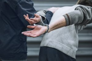 Man bent over in handcuffs being led by officer