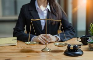 Female lawyer sitting at desk with scales of justice and gavel.