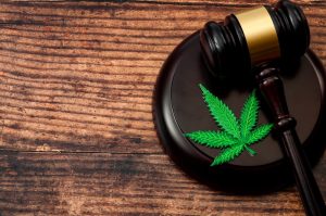 Judge’s gavel resting beside a cannabis leaf on a wooden surface.