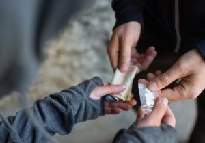 Close-up of a hand-to-hand drug exchange involving small packets.