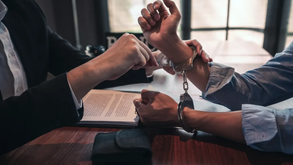 Lawyer meeting with a handcuffed client at a desk.