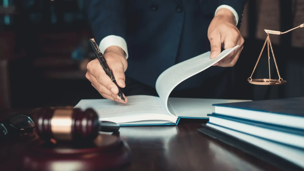 Person in a suit writing in a book with a gavel on the desk.