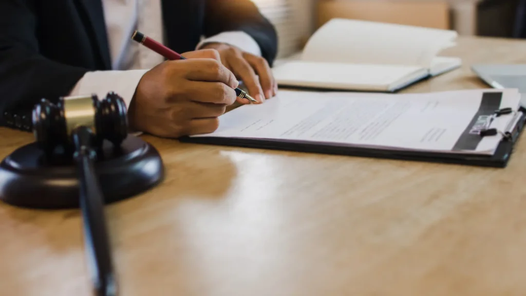 Close-up of a person signing a legal document with a gavel next to them.